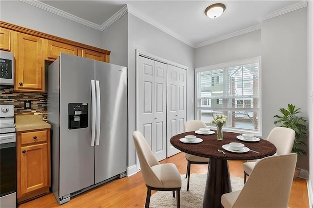 kitchen with appliances with stainless steel finishes, light wood-type flooring, ornamental molding, and backsplash