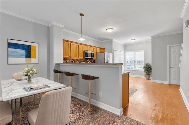 kitchen featuring appliances with stainless steel finishes, light wood finished floors, brown cabinetry, a kitchen bar, and tasteful backsplash