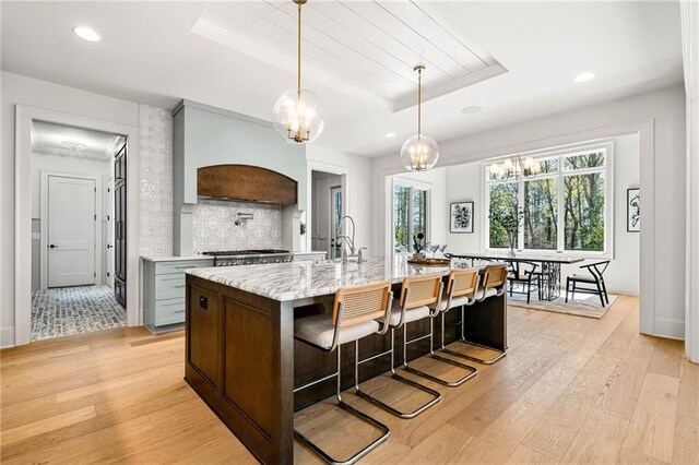 kitchen featuring premium range hood, light hardwood / wood-style floors, stainless steel stove, light stone counters, and sink