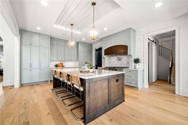 605 Claxton Ln, Milton, GA 30004 - kitchen featuring a tray ceiling, gray cabinetry, light wood-style flooring, custom range hood, and arched walkways