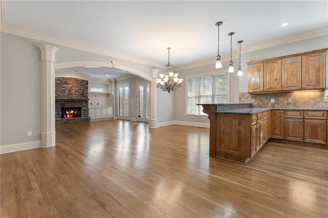 kitchen with hanging light fixtures, kitchen peninsula, a stone fireplace, crown molding, and hardwood / wood-style floors