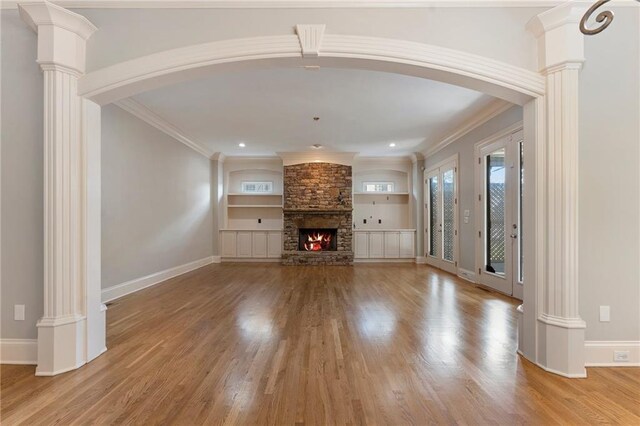 unfurnished living room with a stone fireplace, ornamental molding, light hardwood / wood-style flooring, and decorative columns