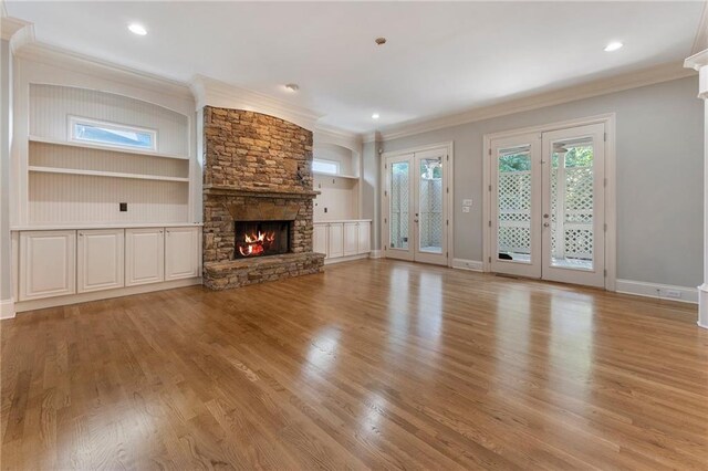 unfurnished living room featuring ornamental molding, light wood-type flooring, a fireplace, and french doors