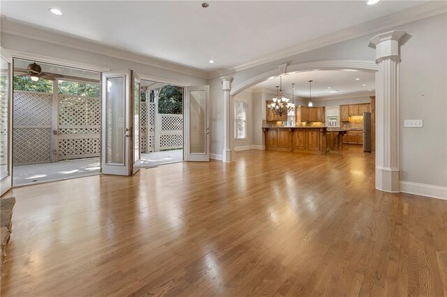 unfurnished living room with ceiling fan with notable chandelier, ornamental molding, light hardwood / wood-style flooring, and ornate columns