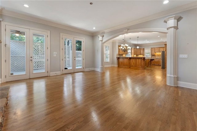 unfurnished living room featuring french doors, light hardwood / wood-style flooring, crown molding, and ornate columns