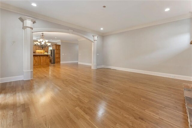 unfurnished living room featuring a chandelier, crown molding, hardwood / wood-style floors, and decorative columns