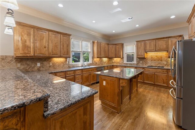 kitchen featuring a center island, stainless steel appliances, light hardwood / wood-style floors, ornamental molding, and decorative light fixtures