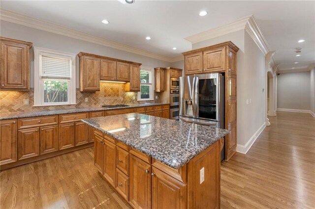 kitchen with backsplash, dark stone counters, a center island, light wood-type flooring, and crown molding