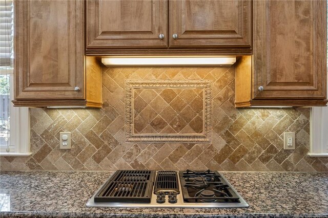 room details with decorative backsplash, dark stone counters, and stainless steel gas stovetop