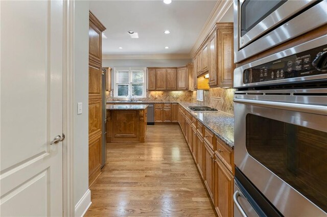 kitchen featuring ornamental molding, a kitchen island, stone counters, appliances with stainless steel finishes, and light wood-type flooring