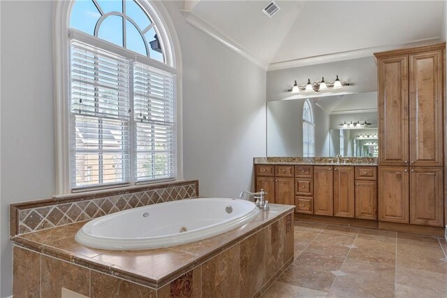 bathroom featuring ornamental molding, vaulted ceiling, vanity, and tiled bath