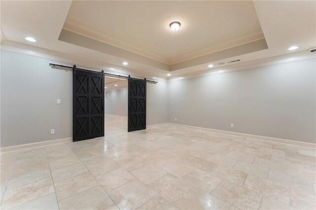 spare room with a barn door, ornamental molding, and a tray ceiling