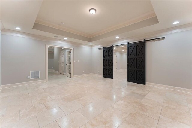 empty room with a barn door, ornamental molding, and a tray ceiling