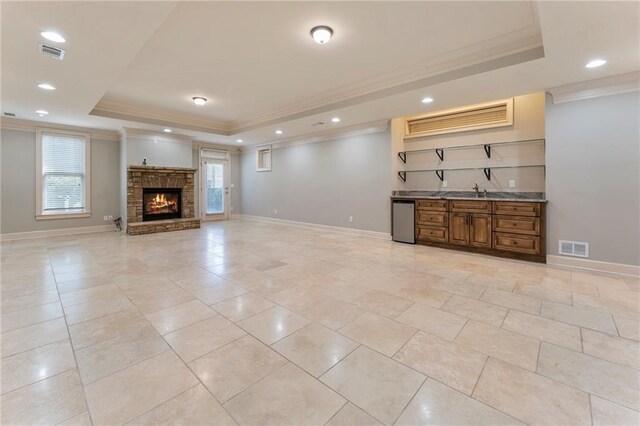 tiled living room with ornamental molding, a tray ceiling, and a stone fireplace