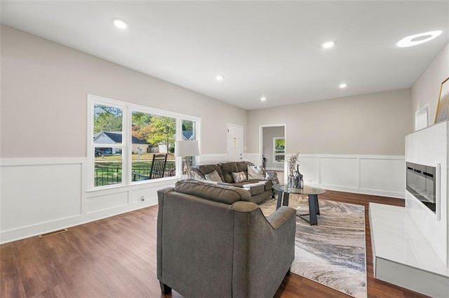 living area with dark wood-style flooring, a fireplace with flush hearth, visible vents, a decorative wall, and wainscoting