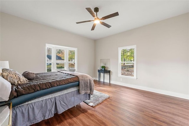 bedroom with multiple windows, ceiling fan, wood finished floors, and baseboards