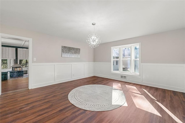 interior space with wood finished floors, a chandelier, a wainscoted wall, visible vents, and a wood stove
