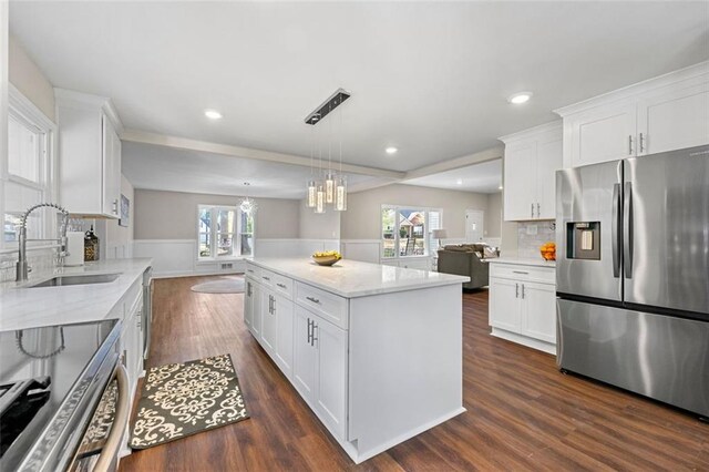kitchen featuring white cabinets, a sink, stainless steel appliances, open floor plan, and backsplash