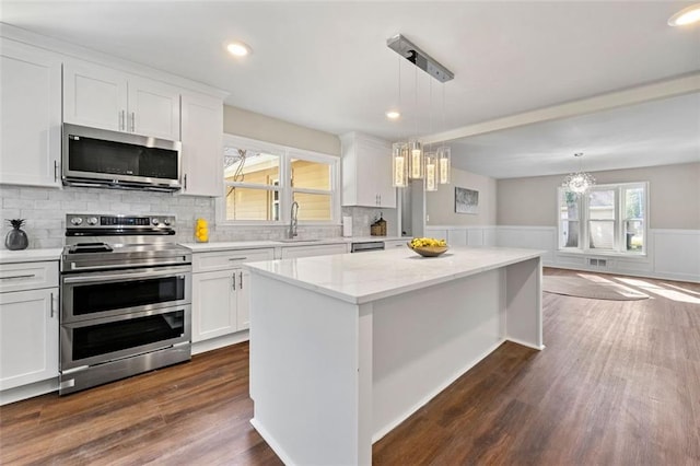kitchen with a chandelier, white cabinets, stainless steel appliances, and a wainscoted wall
