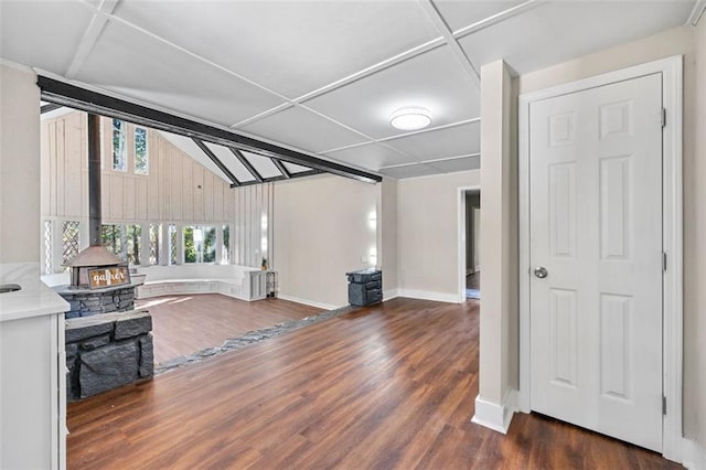 unfurnished living room featuring lofted ceiling with beams, a wood stove, wood finished floors, and baseboards
