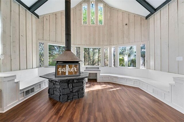 living area with a wood stove, visible vents, lofted ceiling with beams, wooden walls, and wood finished floors