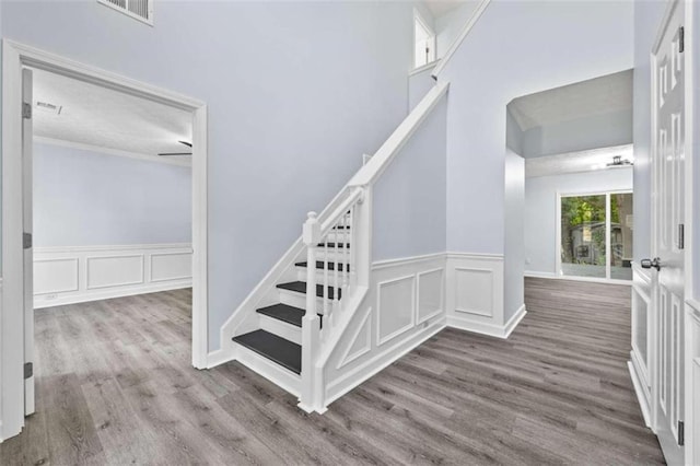 staircase featuring a high ceiling, ornamental molding, and hardwood / wood-style flooring