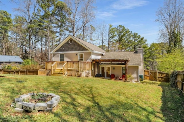 back of property with roof with shingles, a chimney, a lawn, a deck, and a fenced backyard