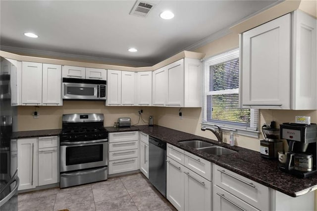 kitchen featuring dark stone countertops, stainless steel appliances, crown molding, a sink, and recessed lighting