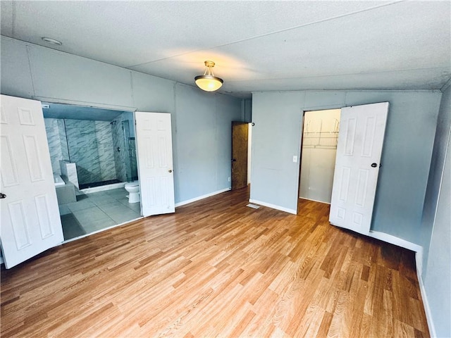 unfurnished bedroom featuring ensuite bathroom, light wood-type flooring, a closet, and a spacious closet
