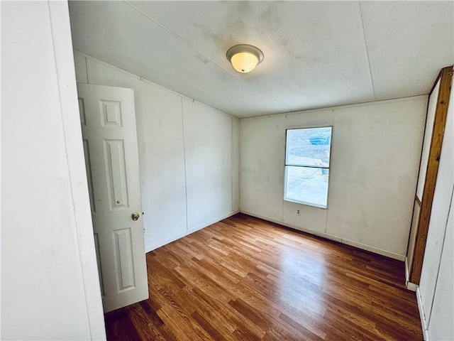 empty room with lofted ceiling, a textured ceiling, and hardwood / wood-style floors