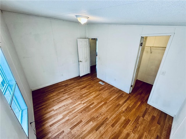 unfurnished bedroom featuring a walk in closet, a closet, hardwood / wood-style floors, and a textured ceiling