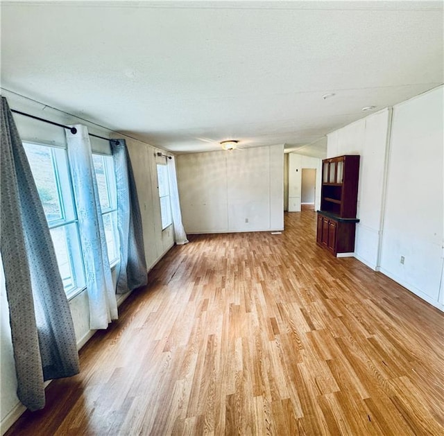 empty room with light wood-type flooring, a textured ceiling, and plenty of natural light