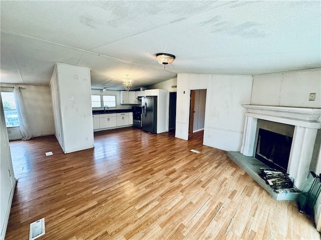 unfurnished living room with sink, light wood-type flooring, a textured ceiling, and plenty of natural light