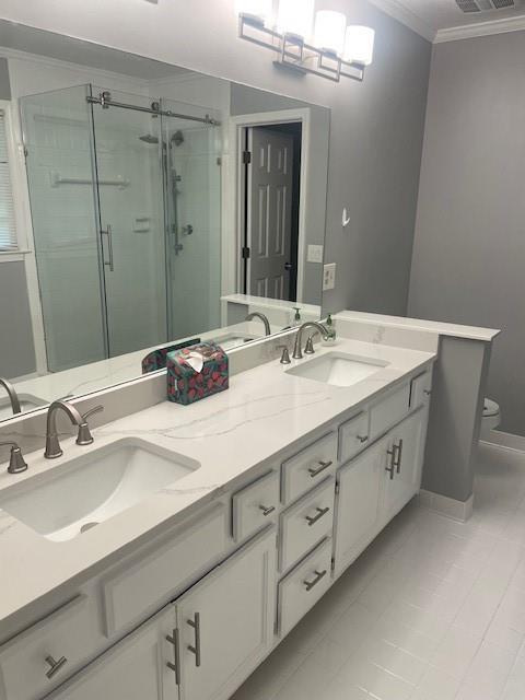 bathroom with toilet, ornamental molding, a sink, and a stall shower