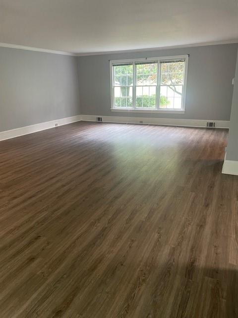 spare room with baseboards, ornamental molding, and dark wood finished floors