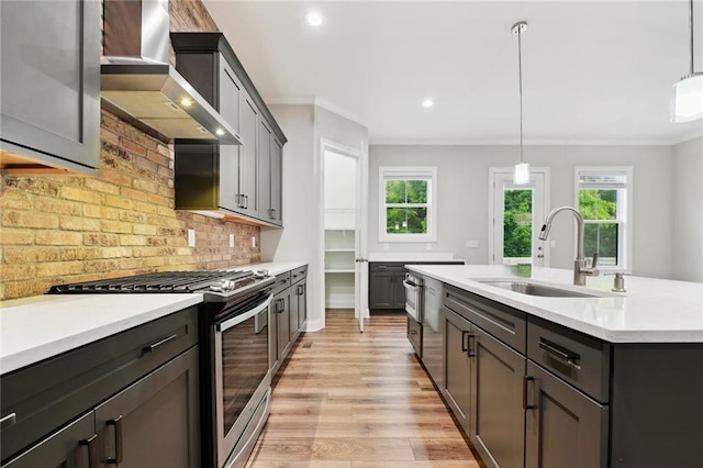 kitchen with light countertops, ornamental molding, stainless steel gas range, wall chimney exhaust hood, and a sink