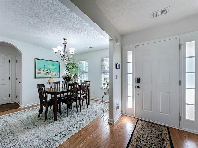 entryway with a textured ceiling, visible vents, wood finished floors, and arched walkways