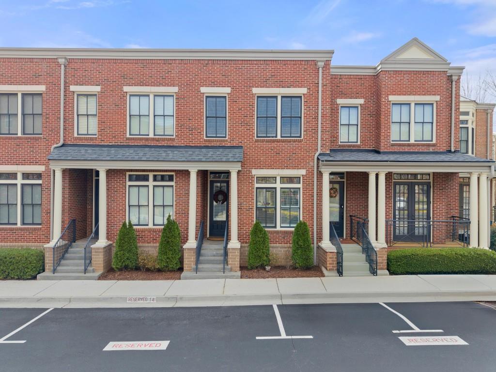 townhome / multi-family property featuring uncovered parking, brick siding, and roof with shingles