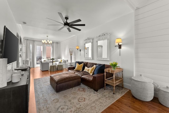 living area featuring wooden walls, wood finished floors, and ceiling fan with notable chandelier