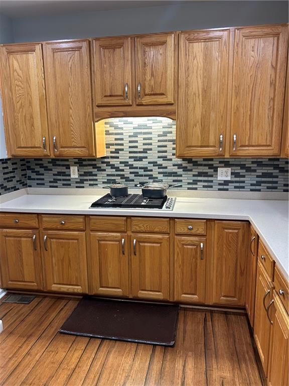 kitchen with dark wood finished floors, gas cooktop, brown cabinetry, and tasteful backsplash