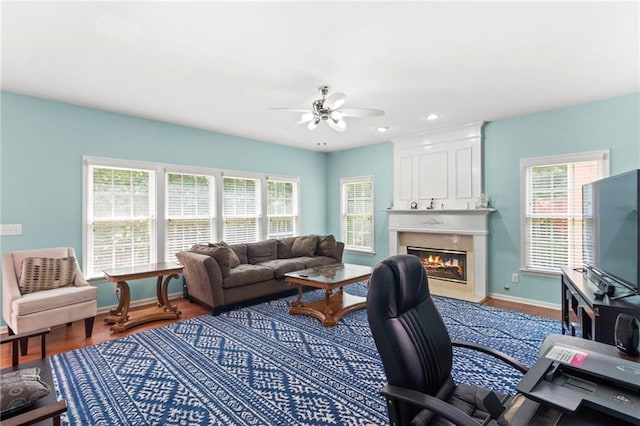 living area featuring wood finished floors, a fireplace, baseboards, and ceiling fan