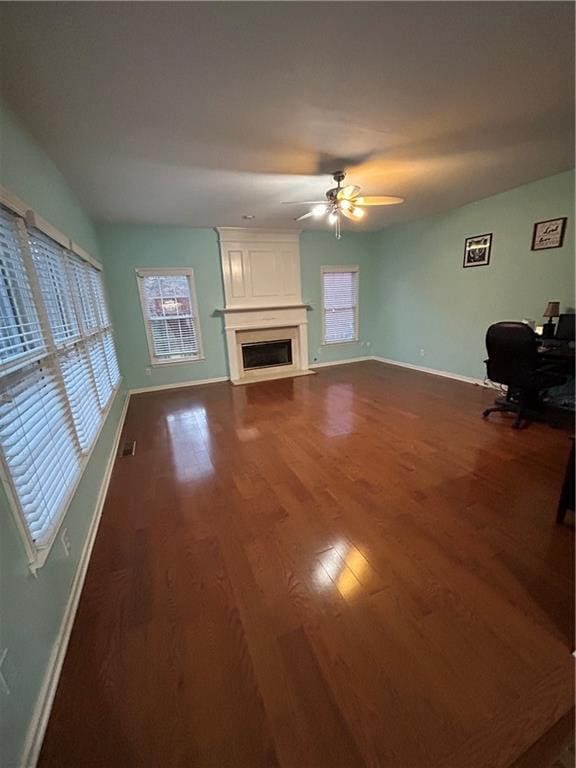 unfurnished living room with a fireplace, dark wood-style floors, baseboards, and ceiling fan