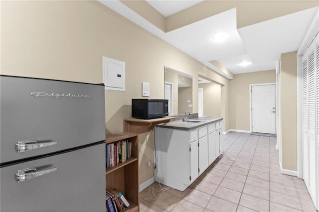 kitchen featuring baseboards, black microwave, electric panel, light tile patterned floors, and white cabinetry