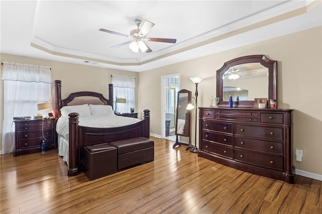 bedroom featuring a ceiling fan, a raised ceiling, baseboards, and wood finished floors