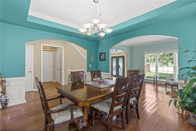 dining area featuring wood finished floors, arched walkways, a raised ceiling, and a chandelier