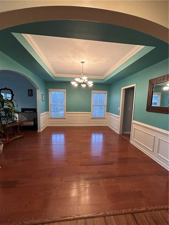 unfurnished dining area with wood finished floors, a raised ceiling, and a chandelier