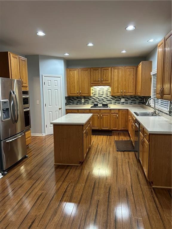 kitchen with brown cabinets, a sink, dark wood-type flooring, appliances with stainless steel finishes, and tasteful backsplash