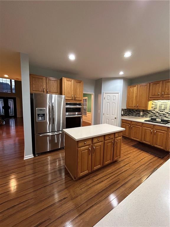 kitchen with dark wood-style flooring, decorative backsplash, light countertops, appliances with stainless steel finishes, and a center island