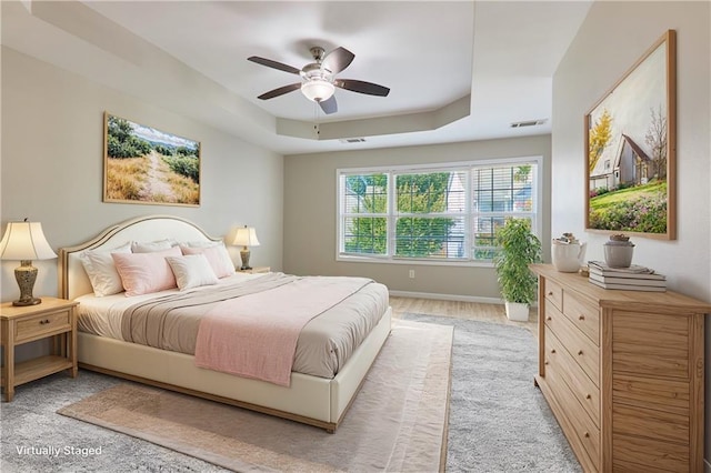 bedroom featuring a raised ceiling, ceiling fan, and light wood-type flooring