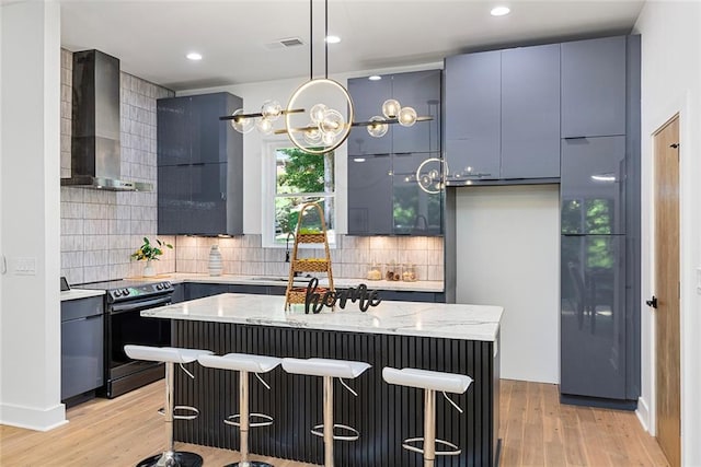 kitchen with a kitchen bar, electric range, decorative light fixtures, wall chimney exhaust hood, and a center island